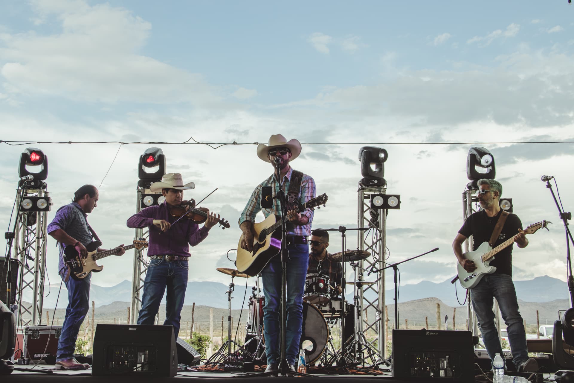 Banda tocando en vivo en el escenario con las montañas del desierto de fondo